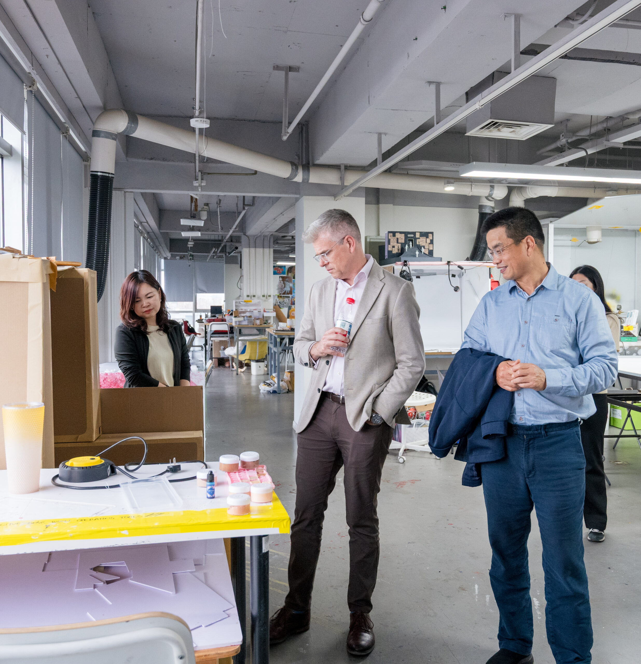 两位学生在工作车间参观，工作台上有材料和工具